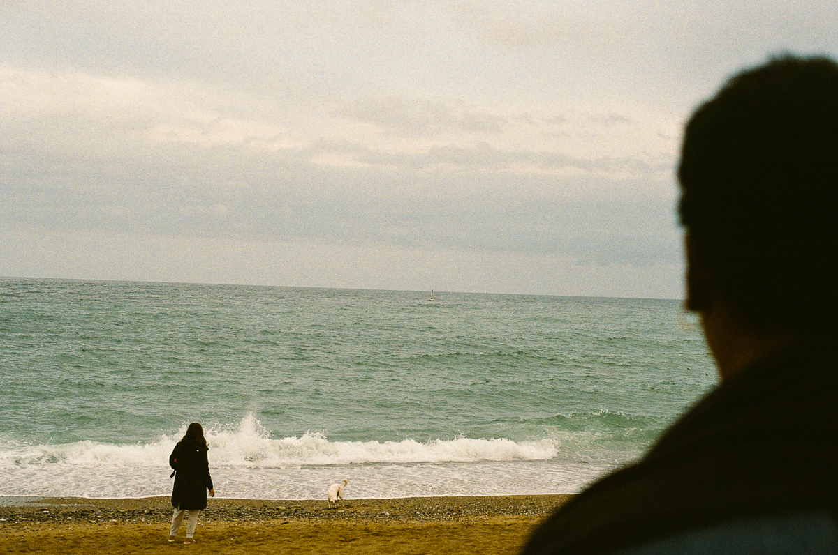 Au loin, une femme et son chien sur la Barceloneta face &agrave; la mer